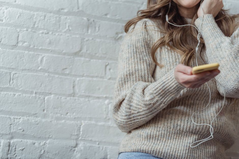 pexels-6954219 person creating playlists on phone with headphones cozy home lifestyle