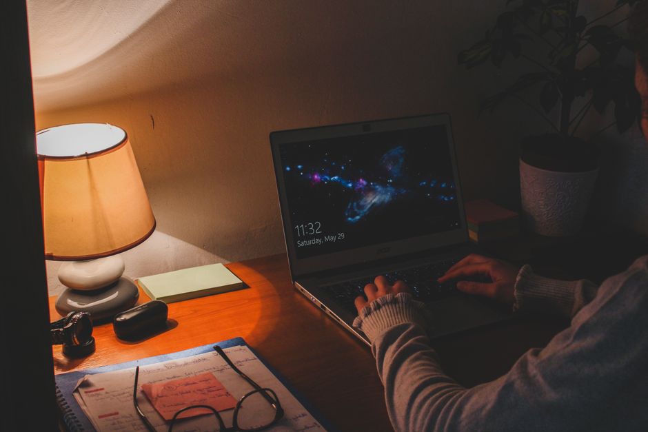 person working at laptop with warm desk lamp and stretching in home office evening
