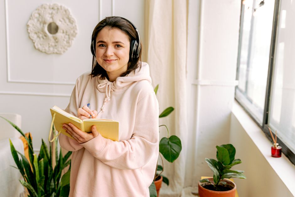 person listening to music with headphones journaling in a cozy living room